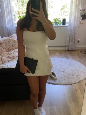 Vit axelbandslös kortklänning - Snygg axelbandslös kortklänning i vitt med snygga volangdetaljer. Klänningen har en figurnära passform och är perfekt för dig som vill sticka ut. Vill köpa ny klänning inför skolavslutningen därför vill jag sälja, har använt ENDAST en gång och är från Ohpolly. Storlek 6 alltså motsvarar XS 