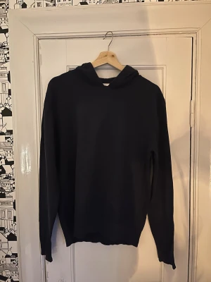 Marinblå hoodie med huva - En enkel och stilren marinblå hoodie med huva och långa ärmar. Hoodien har en klassisk passform och är tillverkad i ett mjukt material som passar perfekt för en avslappnad look. Inga synliga loggor eller mönster, bara clean och snygg.