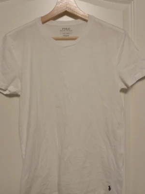 Vit t-shirt från Polo Ralph Lauren - Klassisk vit t-shirt från Polo Ralph Lauren med liten broderad logga nere vid fållen. T-shirten har rund hals och korta ärmar, perfekt basic-plagg till garderoben. Tillverkad i mjuk bomull för skön känsla.