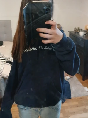 Mörkblå tröja - Mysig mörkblå hoodie med vit text över bröstet i snygg skrivstil. Hoodien har en klassisk huva och en stor magficka framtill. Perfekt för en chill och avslappnad stil. Passar till jeans eller mjukisbyxor för en casual look.