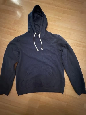 Mörkblå hoodie från Pier One - En stilren mörkblå hoodie från Pier One med klassisk känguruficka och vita dragsnören i huvan. Hoodien har långa ärmar och är gjord i mjukt material som passar perfekt för chill dagar. Enkel och clean design utan tryck eller logga på framsidan.