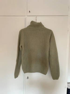 Beige/grön stickad tröja  - Säljer en beige/grön stickad tröja med grov ribbstickning och lång ärm. Tröjan har en hög polokrage och avslappnad passform, perfekt för kyliga dagar. 