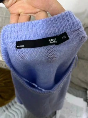 Blålilla stickad tröja - En stilren ljuslila stickad tröja med rund halsringning och långa ärmar. Tröjan har en rak passform och är tillverkad i ett mjukt, tunt material som känns skönt mot huden. Perfekt att matcha med jeans eller kjol för en avslappnad look.