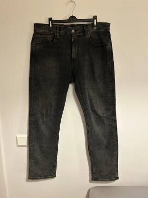 Svartagråa jeans från Levi's - Säljer ett par svarta raka jeans från Levi's modell 502 med klassisk femficksdesign och knappgylf. Jeansen har en tvättad look och är tillverkade i slitstark denim. Passformen är tapered fit. Passar utmärkt med ett par snygga sneakers och en skjorta exempelvis!
