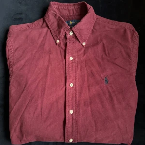 Vinröd skjorta från Ralph Lauren - Klassisk vinröd Oxford skjorta från Ralph Lauren med button-down krage och broderad logga på bröstet. Slim fit. 