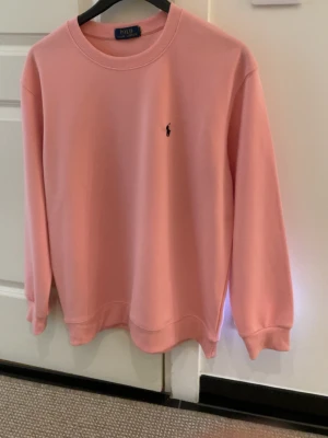Rosa sweatshirt från Polo Ralph Lauren - Säljer en snygg rosa sweatshirt från Polo Ralph Lauren med klassisk rund halsringning och den ikoniska lilla broderade loggan på bröstet. Tröjan har långa ärmar och ribbade muddar vid ärmslut och nederkant. Perfekt för en avslappnad och stilren look.