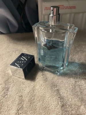 Ad Vatim Afteram parfym - Snygg parfymflaska från Ad Vatim med ljusblå vätska och silverfärgat lock. Flaskan har en modern, kantig design med vingar tryckta på framsidan. Perfekt för dig som gillar stilrena och unika dofter.