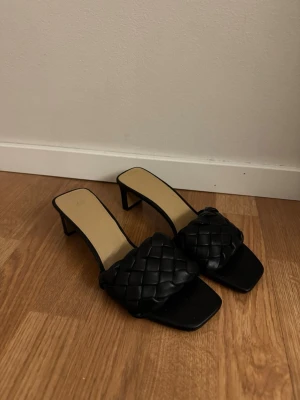 Svarta flätade sandaler med klack - Säljer ett par svarta sandaler från H&M med låg klack och fyrkantig tå. Ovandelen har en bred, flätad rem i syntetmaterial som ger en trendig look. Perfekta till sommarens outfits och lätta att matcha med allt.
