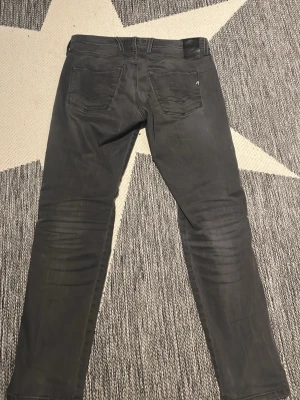 Gråa slim fit jeans från Replay - Snygga gråa slim fit jeans från Replay med slitningar på framsidan och klassiska fem fickor. Jeansen har en modern passform och detaljerade sömmar på bakfickorna. Perfekta för en trendig och avslappnad stil.