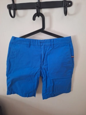 Blå shorts från Tommy Hilfiger - Snygga blå shorts från Tommy Hilfiger med klassisk passform och bälteshällor. Tillverkade i mjuk bomull och har diskret logodetalj vid fickan. Perfekta för varma dagar och enkel att matcha med olika stilar.