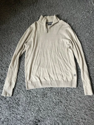 Beige half zip tröja Jack & Jones - Beige half zip tröja från Jack & Jones med halv dragkedja och hög krage. Tröjan har lång ärm och ribbade muddar vid ärmslut och nederkant. Perfekt för lager-på-lager och enkel att matcha med jeans eller chinos.