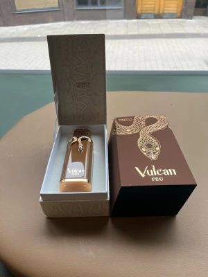 Vulcan Feu exklusiv parfym - Lyxig parfym från Vulcan i en elegant guld- och bronsfärgad flaska med ormdekor. Kommer i en snygg brun ask med gulddetaljer och ormmönster. Flaskan har exklusiv design och känns riktigt premium – perfekt för dig som gillar unika dofter och snygga förpackningar.