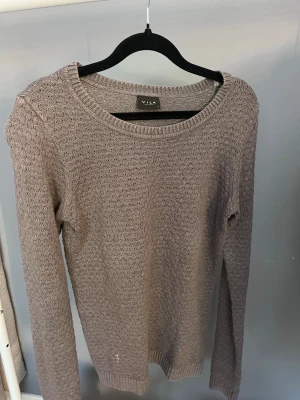 Beige stickad tröja från Vila - Säljer en beige stickad tröja från Vila med rund halsringning och lång ärm. Tröjan har ett diskret strukturmönster och ribbade muddar vid ärmslut och nederkant. Perfekt för lager på lager och enkel att matcha med olika stilar.
