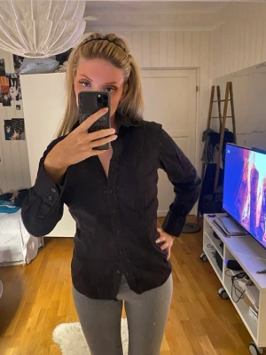 Svart skjorta med knappar - Stilren svart skjorta med klassisk krage och knäppning framtill. Skjortan har lång ärm och figurnära passform, perfekt för en clean och enkel look. Passar till både jeans och kostymbyxor.