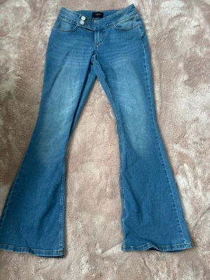 Blå bootcut jeans från Vero Moda - Snygga blå bootcut jeans från Vero Moda med dubbla knappar i midjan och klassisk femficksdesign. Jeansen har en lätt tvättad look och är tillverkade i bomull med lite stretch för extra komfort. Priset går att diskutera💕