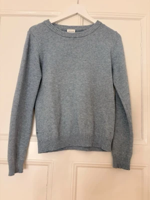 Ljusblå stickad tröja från VILA - Mysig ljusblå stickad tröja från VILA med rund halsringning och ribbade muddar vid ärmslut och nederkant. Tröjan har en enkel och klassisk design som passar perfekt till jeans eller kjol. Materialet känns mjukt och behagligt mot huden. Den är lite nopprig och har fått ett pytte litet hål 