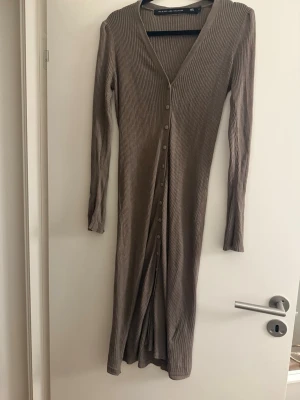 Ribbad brun långklänning/kofta - Långärmad ribbad klänning i brun nyans från Lager157. Klänningen har v-ringning och knappar hela vägen framtill, vilket ger en snygg och enkel look. Kan även användas som kofta. Tillverkad i mjukt material som sitter skönt på kroppen. Perfekt för dig som gillar stilrena och bekväma plagg.