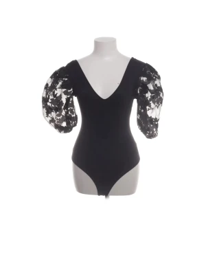 Svart body med puffärmar från Zara - Trendig svart body från Zara med djup V-ringning och stora puffärmar i transparent mesh med blommigt mönster. Kroppsnära passform och knäppning nedtill. Perfekt för dig som vill ha en statement-piece i garderoben.