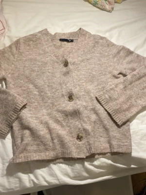 Beige kofta med stora knappar - Mysig beige kofta från lager 157 med tre stora bruna knappar framtill. Koftan har v-ringning, långa ärmar och ribbade muddar vid ärmslut och nederkant. Perfekt för lager-på-lager-stil.