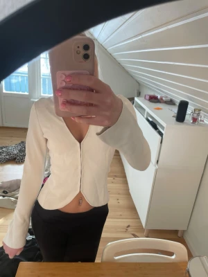 Vit v-ringad topp från Zara - Populär snygg vit topp från Zara med v-ringning och lång ärm. Modellen är figurnära och har en lätt croppad passform. Perfekt att styla med både jeans och kjol. Materialet känns mjukt och stretchigt, vilket gör den bekväm att bära hela dagen.