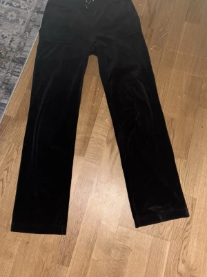 Svarta juicy byxor  - Säljer ett par svarta mjukisbyxor i mjuk velour med raka ben och resår i midjan. Byxorna har två fickor bak med knappdetaljer. Perfekta för en chill och avslappnad stil. De är i storlek S och pris kan diskuteras 💕