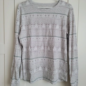 Grå långärmad tröja och byxor med mönster - Säljer en grå långärmad tröja och byxor med ett subtilt mönster i vitt, grönt och rött. Tröjan har en rund halsringning och är perfekt för kyligare dagar. Den är både stilren och bekväm.