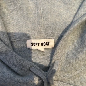 Blå/grön hoodie från Soft Goat - Mysig grå hoodie från Soft Goat i kashmir. Perfekt för kyliga dagar med sin mjuka och bekväma passform. Den har en klassisk huva med dragsko och ribbade muddar vid ärmslut och nederkant.