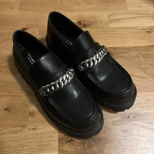 Svarta loafers från Vagabond 37 - Snygga svarta loafers från Vagabond med en robust sula och dekorativ kedjedetalj över vristen. 