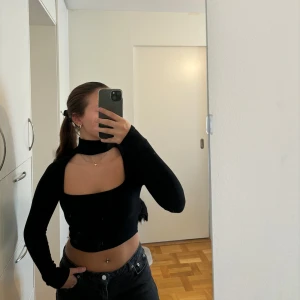 Svart långärmad topp - Snygg svart ”croppad” topp med långa ärmar och en cut out med en hög krage som detalj. Passar till olika tillfällen och är endast använd 1 gång!