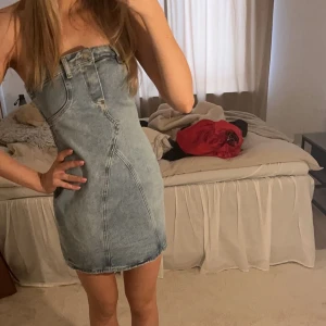 Axelbandslös jeansklänning - Trendig axelbandslös jeansklänning i en ljus tvätt. Perfekt för en avslappnad stil med en figurnära passform. Klänningen har dekorativa sömmar och en kort längd som ger en modern look.