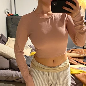 Rosa croppad topp med öppen rygg - Säljer en snygg rosa croppad topp med långärmad design och öppen rygg. Toppen har en knytning i ryggen som ger en unik look. Perfekt för en trendig stil.
