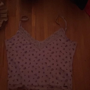 Ljuslila blommig linnetopp - Söt ljuslila linnetopp med små blommor och spetsdetaljer vid halsringningen. Toppen har smala axelband och en lätt vågig nederkant.