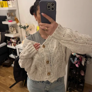 Beige stickad kofta med knappar - Mysig beige stickad kofta med stora träknappar. Koftan har ett fint flätmönster och långa ärmar. Lite oversized och inte sån stickig känsla i materialet. Jätte fin att ha nu eller att ba slänga över något på sommarkvällar. Helt ny, aldrig användd med pristagg fortfarande på.