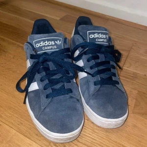 Blå Adidas Campus sneakers - Säljer ett par snygga blå Adidas Campus sneakers med vita detaljer och snörning. Perfekta för en avslappnad stil. Tillverkade i mocka för en klassisk look. Har bara använt dem fåtal gånger eftersom de är för små för mig. Orginalpris är 1200kr