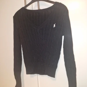 kabelstickad tröja  - Snygg svart stickad tröja från Ralph Lauren med v-ringning och kabelstickat mönster. Lappen i nacken är tyvärr avklippt men jag skulle säga att tröjan passar S  PRIS GÅR ALLTID ATT DISKUTERA