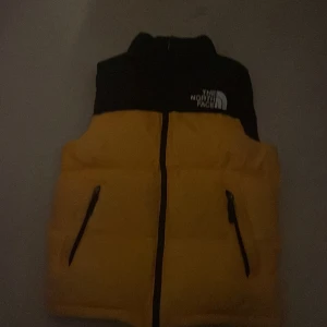 Gul och svart dunväst från The North Face - Säljer denna Northug face väst då den är för liten den är i L junior men sitter som s den är köpt på the north face hemsida nypris 2399kr jag säljer den för 899kr