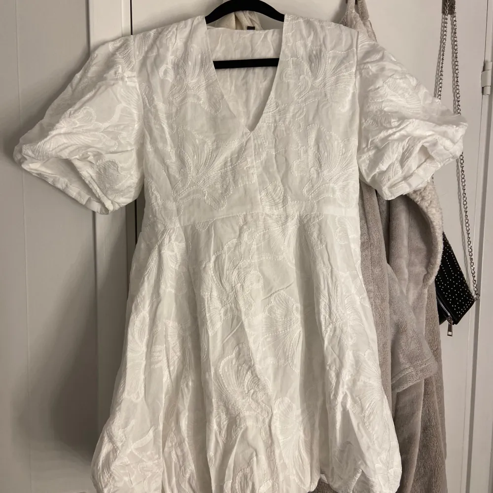 Säljer en vit klänning med puffiga kortärmar och v-ringning. Klänningen har ett vackert broderat mönster och en luftig passform. Perfekt för dig som ledar efter en studentklänning! Helt oanvänd om ny! Nypris: 499kr. Mekot.