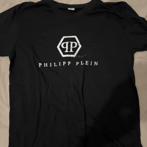 Svart t-shirt från Philipp Plein - Snygg svart t-shirt från Philipp Plein med deras ikoniska logotyp tryckt i vitt på framsidan. Perfekt för en stilren och modern look.