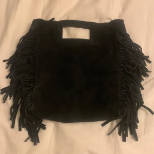 Svart skinnväska med fransar - Snygg svart skinnväska med fransar på sidorna och praktiskt handtag. Tillverkad i Italien, Perfekt för en trendig look.