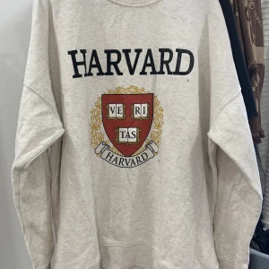 Beige sweatshirt med Harvard-tryck från H&M - Säljer en beige sweatshirt från H&M med ett stort Harvard-tryck på framsidan. Tröjan har långa ärmar och en rund halsringning. Perfekt för en avslappnad stil med en touch av akademisk känsla.