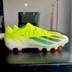 Neongula fotbollsskor från Adidas - Snygga neongula fotbollsskor från Adidas med svarta och vita detaljer. Skorna har en lätt och smidig design med snörning och en greppvänlig sula i orange och vit. Perfekta för att dominera på planen!