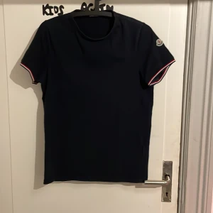 Svart t-shirt från Moncler - Snygg blå t-shirt från Moncler med korta ärmar och en broderad logga på ärmen. Perfekt för en stilren look. Kan gå ner i pris vid snabb affär
