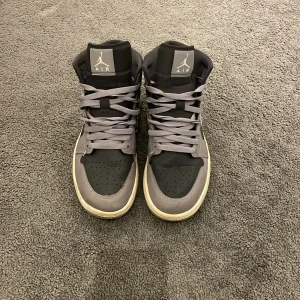 Nike Air Jordans i grått och svart - Snygga Nike Air Jordans i grått och svart med klassisk design. Skorna har snörning och en vit sula som ger en stilren kontrast. Perfekta för dig som vill ha en ikonisk sneaker med hög komfort. Pris kan diskuteras