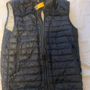 Svart dunväst från Parajumpers - Snygg svart dunväst från Parajumpers med dragkedja framtill och praktiska fickor. Perfekt för lager-på-lager under kyliga dagar. Västen har en stilren design med quiltade detaljer och en hög krage. Nypris 4299kr mitt pris 1500 men kan diskuteras vid snabb affär 