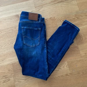 Blåa Jack & Jones jeans - Snygga blå jeans från Jack & Jones med klassisk femficksdesign och en bekväm passform. Perfekta för en avslappnad stil. Märkesdetaljer på baksidan och insidan av midjan storlek W29 L30.