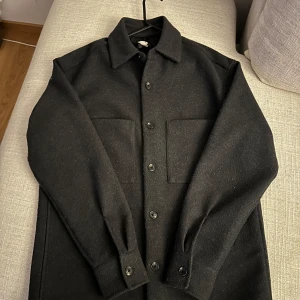 Svart overshirt - Snygg svart overshirt med knappar framtill och två stora bröstfickor. Perfekt för lager-på-lager-stil. Långärmad design med klassisk krage. Köparen står för frakt