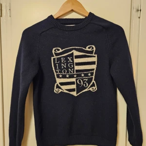 Mörkblå tröja från Lexington - Säljer en snygg mörkblå tröja från Lexington med ett stort emblem på framsidan. Tröjan har långa ärmar och en klassisk rund halsringning. Tröjan är M men är mindre i storleken så passar S kanske XS. Skriv om ni har frågor!