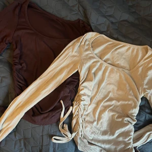 Två ribbade långärmade toppar - Säljer två snygga ribbade toppar med långa ärmar. Den ena är beige och den andra brun, båda med knytning i sidan för en justerbar passform. Perfekta för höst och vår! Säljer båda för 50kr och är i storlek S.