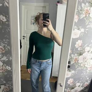 Grön oneshoulder topp - Snygg grön oneshoulder topp med lång ärm. Perfekt för en trendig look. Passar bra till jeans eller kjol.