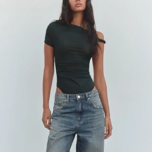 Mörkgrön body - Snygg mörkgrön body från Zara med oneshoulder-design. Den har en tight passform och är lite genomskyndlig i materialet. Helt ny med prislapp kvar!